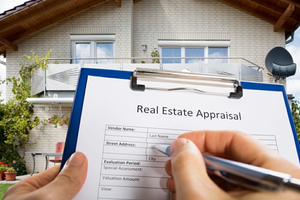 Close-up Of Person Hand Filling Real Estate Appraisal Document In Front Of House